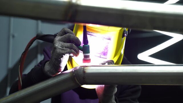 4k video Welder performs argon TIG welding on a custom automotive exhaust pipe using a tungsten electrode for precise fusion, wearing a protective welding helmet.