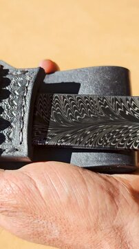 Unsheathing a custom handmade knife with a striking Feather Damascus pattern.