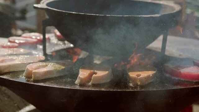 Salmon steak cooking on hot metal grill plate over open fire. Delicious seafood barbecue preparation outdoors. Culinary process of grilling fresh fish for gourmet restaurant dinner feast.