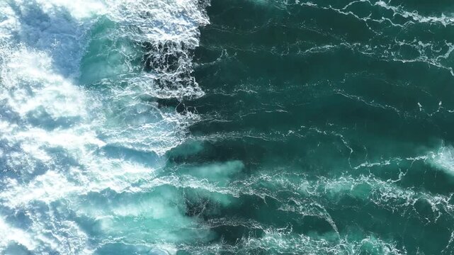 Aerial view of powerful turquoise ocean waves crashing with white foam and surf in the deep blue sea Bali, Indonesia.