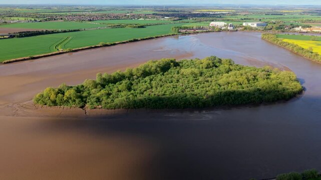 Aerial view of Howden Dyke Island covered in lush green trees on the River Ouse surrounded by rural fields and industrial sites in Goole, England, United Kingdom.