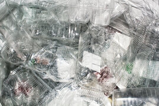 Close-up top view of a pile of empty transparent plastic food containers and clamshell packaging collected for recycling or waste disposal purposes inside a white bag