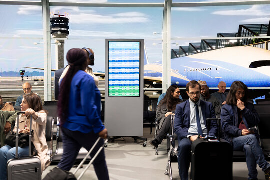 Man and woman carrying trolley in airport terminal, checking flight information on screen. African american couple travelling together to foreign countries, doing city break