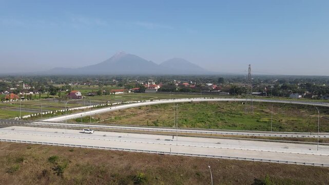 Aerial view of a blue bus driving on a highway interchange with Mount Merapi in the background Klaten, Central Java, Indonesia.