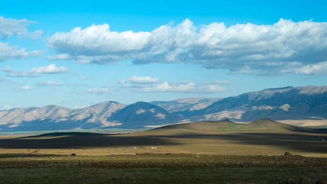 Wide panoramic view of the Middle Atlas Mountains in Morocco with green plains and a blue sky filled with white clouds on a sunny day showcasing a vast natural landscape,