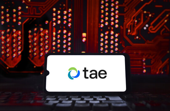 TAE Technologies logo, a fusion energy company, on a smartphone screen with an industrial background.