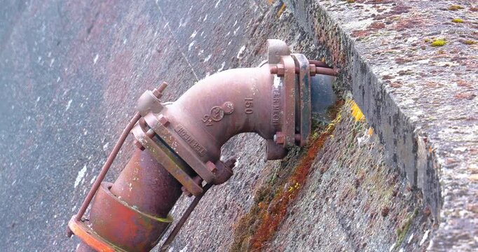 Rusted metal pipe elbow joint mounted on weathered concrete wall