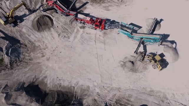 Aerial view of heavy machinery including excavators and conveyors operating in a gravel quarry with piles of sand in Indianapolis, Indiana, United States.