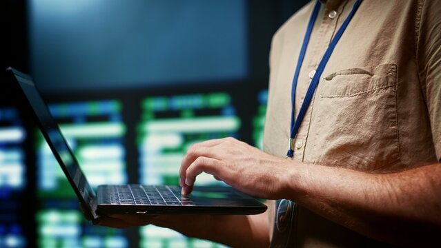 IT developer using laptop to monitor server farm security to protect information access, making sure virus protection software is updated and hackers trying to penetrate systems are rejected, close up