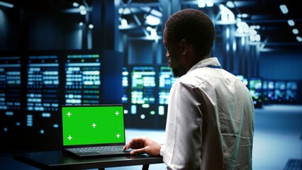 Fototapeta premium Professional examining server cabinets performance trends. Repairman using chroma key laptop to pinpoint data center operational issues arising due to high CPU usage and insufficient memory