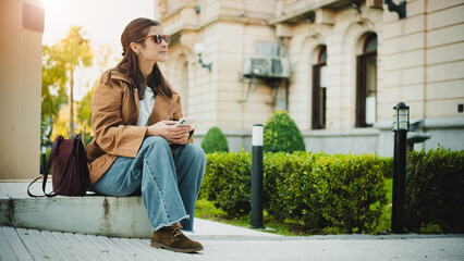 Young woman wearing sunglasses using her smartphone at sunset in the city. Urban technology and modern lifestyle concept. © Emanuel