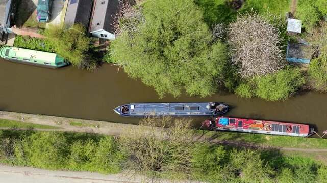 Aerial view of narrowboats moored along a canal with lush green trees and spring blossoms at Barton Marina in Barton-under-Needwood, England, United Kingdom.