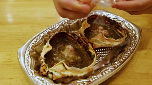 Close up of hands unpacking plastic spoon for eating traditional japanese grilled crab miso dish.