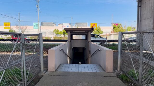 Entrance to pedestrian underpass at railway crossing with moving cars in background.