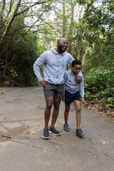 Naklejka premium African American father and son walking on paved woodland trail laughing, wearing gray hoodies