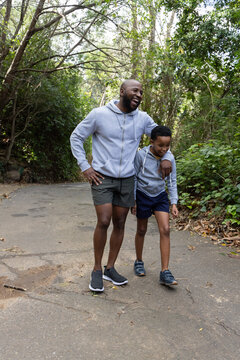 African American father and son walking on paved woodland trail laughing, wearing gray hoodies