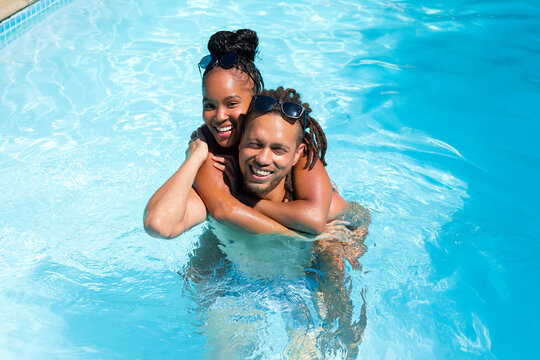African American couple embracing in sunny pool with sunglasses swimwear coping and rippling water