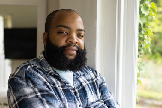 Adult African American man posing at home by white window wearing plaid shirt daylight bathing face