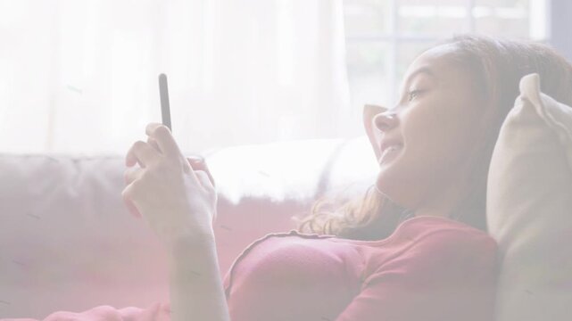 Adult female reclining couch starting tapping smartphone, scrolling tech content, smiling at screen