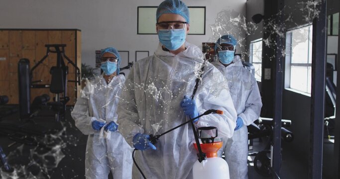 Holding pump sprayer, sanitation tech preparing to spray in gym, wearing protective gear