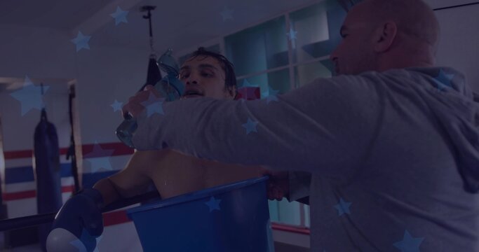 Leaning shirtless boxer breathing on ropes at ring corner, coach handing water bottle, blue bucket
