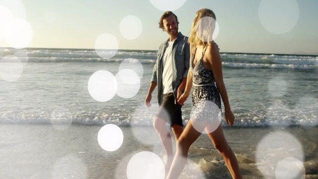 Couple entering shallow surf holding hands, walking shore for travel ad, bokeh drifting over couple