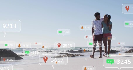 Fototapeta premium Walking couple in casual beachwear walking along wet sand on beach with digital markers, copy space