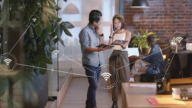 Team consulting reviewing notes in tech woman tapping tab growing WiFi nodes linking plant to desks