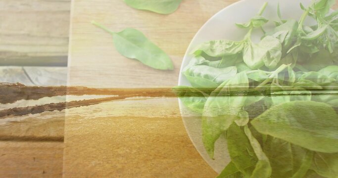 Showing white bowl of green salad leaves sitting on wooden tabletop, shoreline overlay, copy space