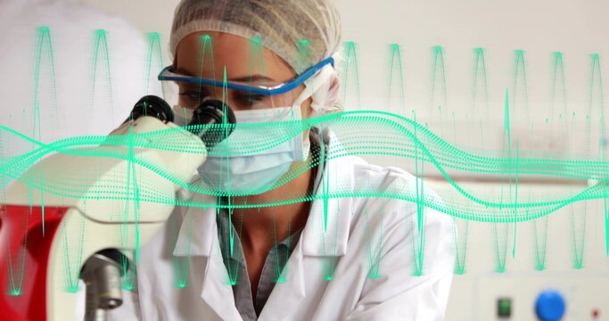 Leaning lab scientist peering into microscope at lab bench, wearing PPE with teal waveform overlay