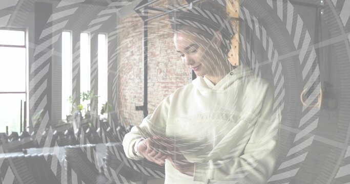 Checking hoodie-clad woman adjusting watch on wrist while standing in loft area, spiral overlay