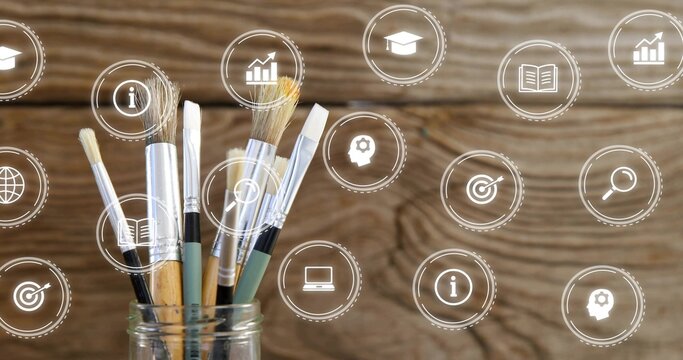Displaying glass jar holding paintbrushes on wooden tabletop, with education icons, copy space