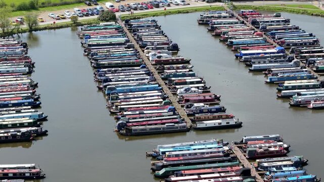 Aerial view of rows of colorful narrowboats moored at Barton Marina with a parking lot in the background in Barton-under-Needwood, England, United Kingdom.