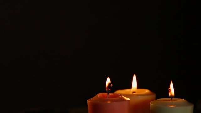 Three colorful magic candle flames calm burning in home interior on black dark background with copy space. Closeup yoga, spa, wellness, relaxation concept. No people	
