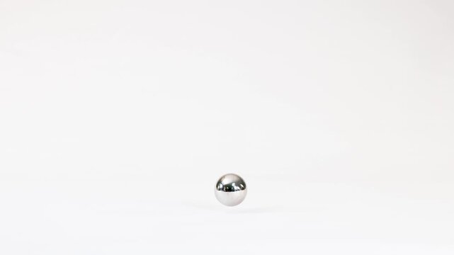 Shiny metal ball falling slowly in slow motion against white background.