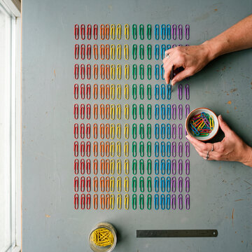 Manos organizando clips de colores en una cuadr&iacute;cula perfecta, concepto de orden.
