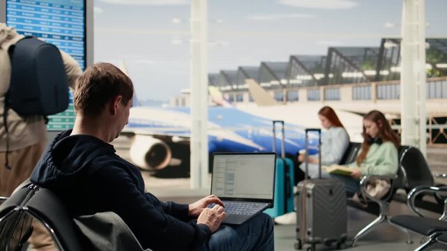 Man digital nomad, focused on programming, system development on laptop, in the airport terminal, surrounded by passengers. Coding and data processing via flexible job mobility.