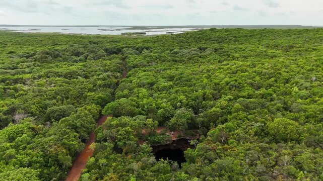 Aerial view of Sapphire Blue Hole surrounded by lush tropical forest and a dirt road in The Bluff Settlement, North Eleuthera, The Bahamas.