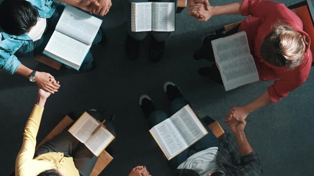 Top down view of diverse people holding hand and sitting in circle with bible book on lap. Aerial view of faithful prayer clasp hand and praying to god with faith, religion conceptional. Symposium.