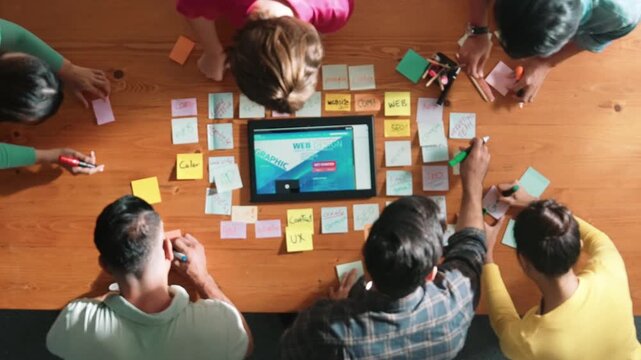 Top down view of programmer brainstorming and planning about web design while looking at tablet wireframe prototype. Aerial view of skilled developer team talking about digital application. Symposium.