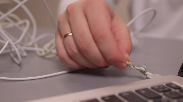 Laptop power cord repair process. Careful examination of frayed laptop connector wires. Closeup view of technician inspecting compromised power cable connections on desk