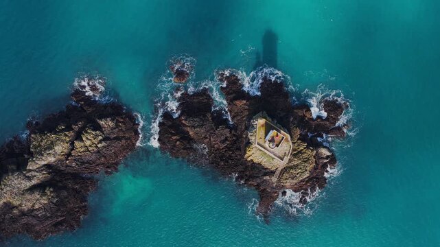 Aerial view of Phare de L'Ost-Pic lighthouse on a rocky islet surrounded by turquoise water in Plouezec, Bretagne, France.