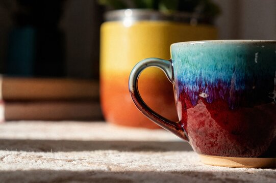 Handmade ceramic coffee mug with colorful glaze on sunlit surface ideal for artisan pottery shop and cozy lifestyle content