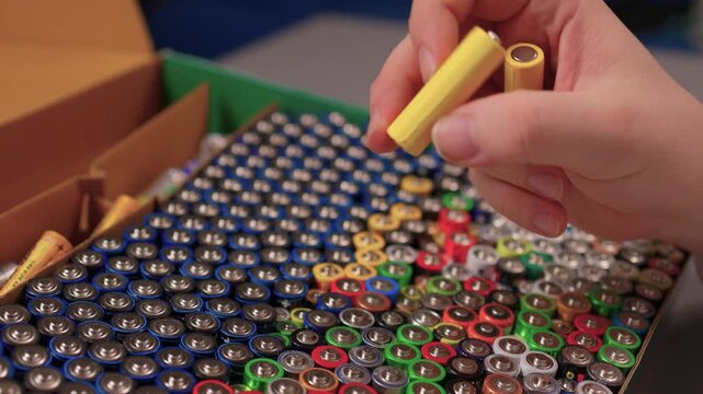 Closeup of individual working with batteries and tools. Workshop scene showing person inspecting and managing various electric power cells with focus on safety and quality