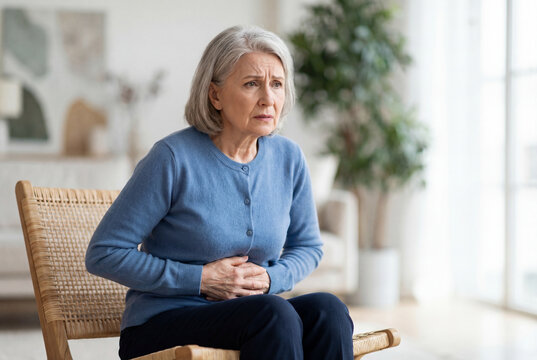 Senior woman suffering from stomach pain on chair