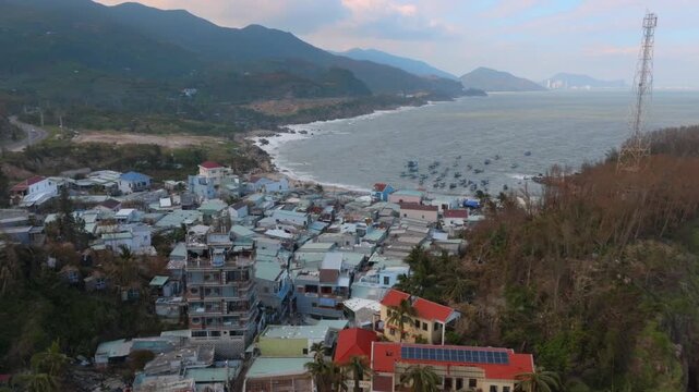 A coastal village iof  Bai Xep, Quy Nhon, Vietnam. shows signs of damage, with boats in the choppy sea and a telecommunications tower overlooking the scene.