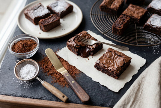Fresh baked dark chocolate fudgy brownies dusted with powdered sugar on a dark slate surface