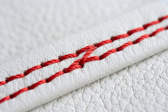 Close up macro view of textured white leather material featuring bright red thread stitching