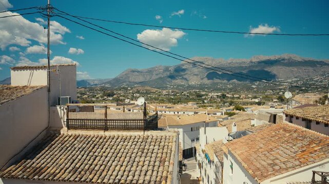 Bright view over traditional rooftops in Altea, Spain, with mountains in the background under a clear blue sky. Warm Mediterranean atmosphere and peaceful village setting.