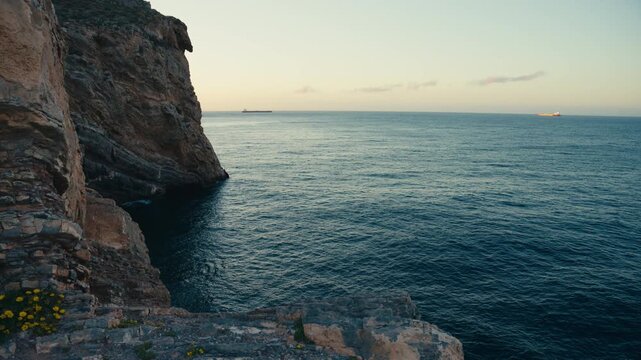 Calm ocean stretches along rugged coastal cliffs during sunset, with distant ships on the horizon creating a peaceful and cinematic seaside atmosphere.